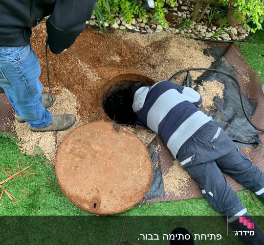 שני אנשים עובדים ליד פתח ביוב עם מכסה עגול